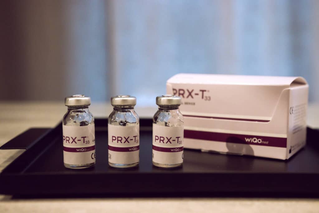 Tre injektionsflaskor med prx-t33 lösning bredvid deras förpackning.