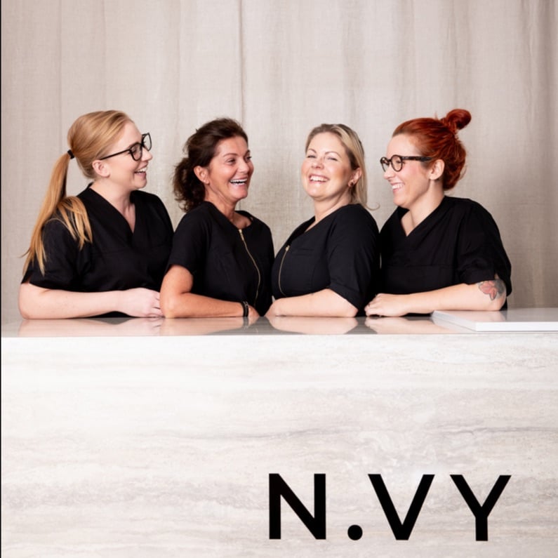 Fyra kvinnor i svarta toppar ler och poserar tillsammans bakom en marmordisk med texten "n.vy" längst ner.