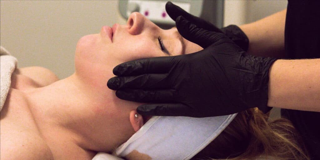 Estetiker som utför en ansiktsbehandling på en avslappnad klient.